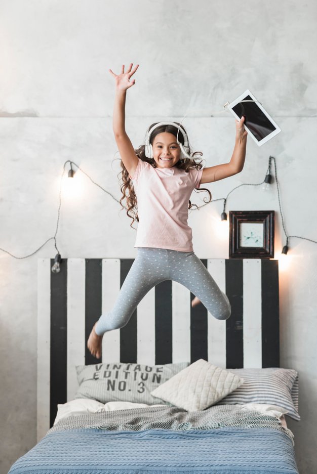 Girl Jumping in A Bed With Her Digital Headphones.
