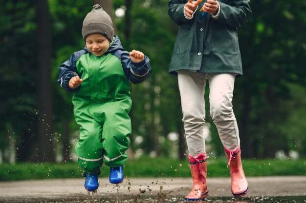 Funny kid in rain boots playing in a rain park Free Photo