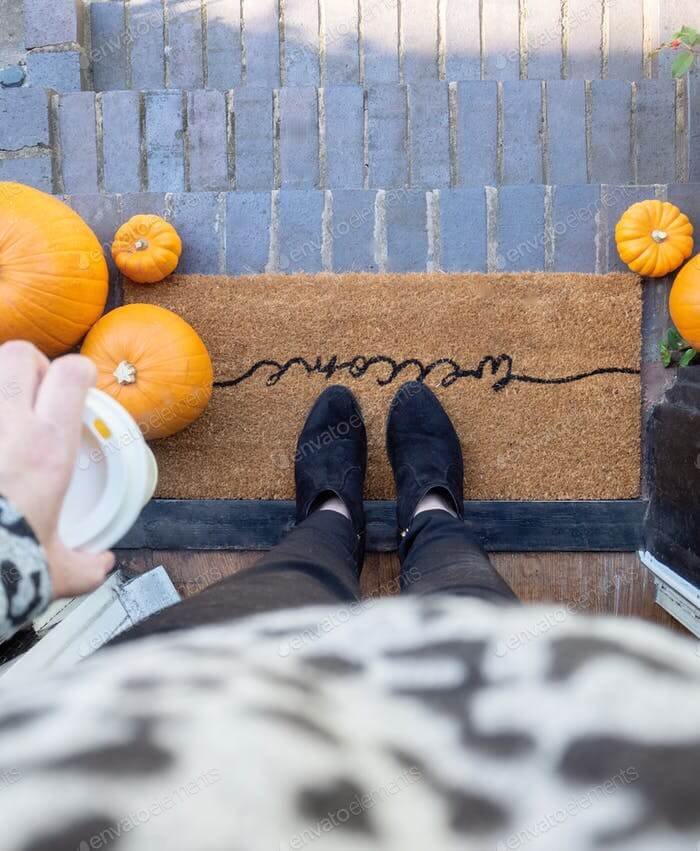 A woman’s feet on a ‘welcome doormat with fall pumpkins on the steps