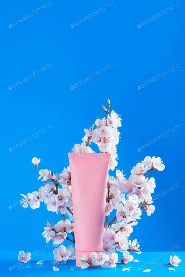Cherry blossom cosmetics concept. Pink creme tube with spring flowers on a sky blue background with