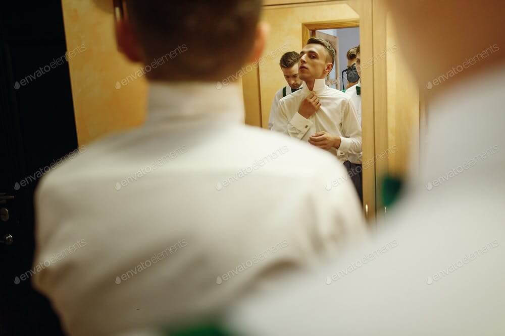 Handsome groomsman friends helping groom put on stylish white shirt